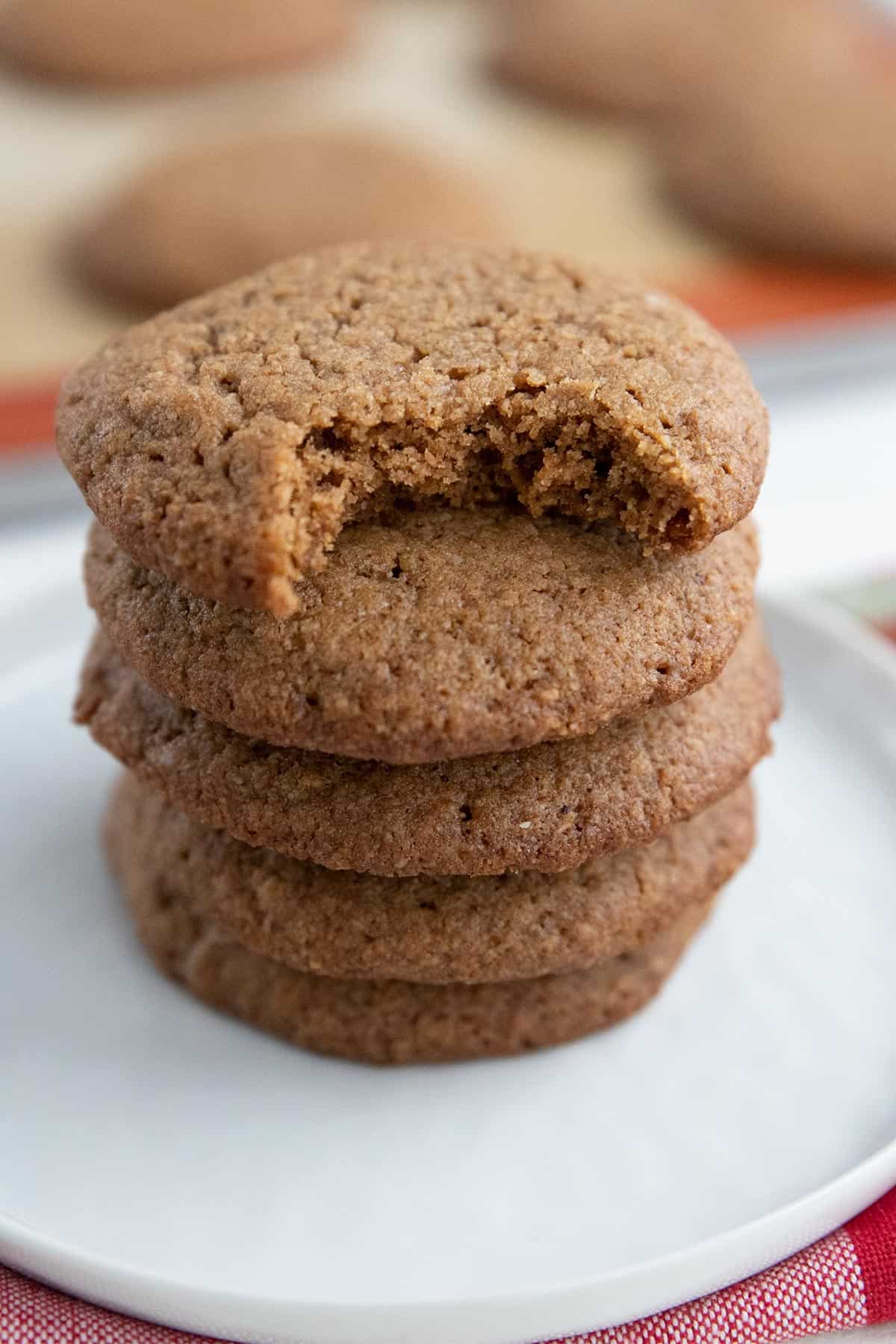Close up shot of a stack of Chewy Keto Ginger Cookies on a white plate, with a bite taken out of the top one.