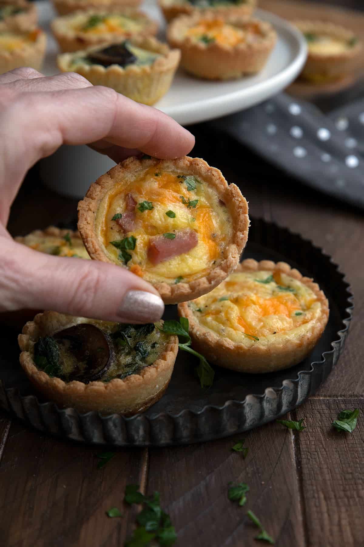 A hand holding up a mini keto ham and cheese quiche.