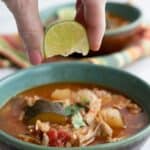 A hand squeezing a wedge of lime into a bowl of keto pork stew.