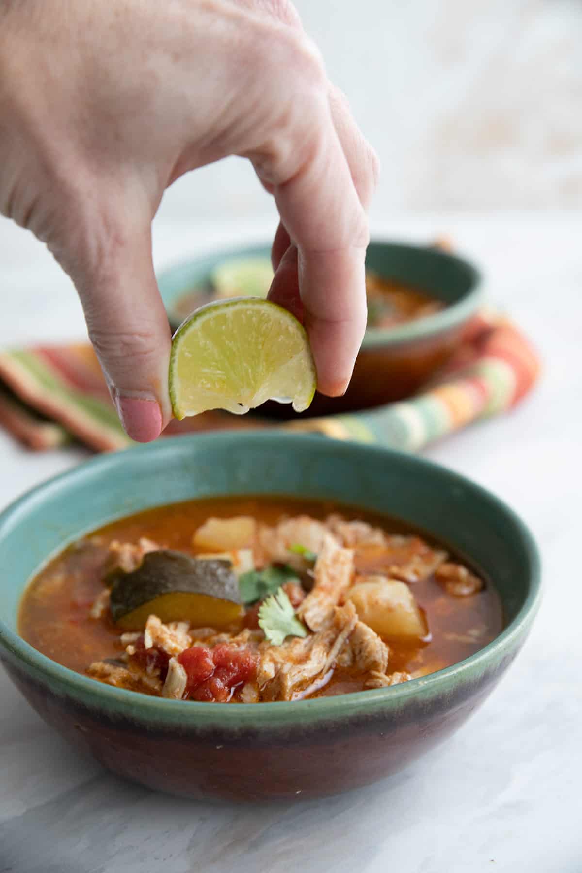 A hand squeezing lime into a bowl of southwestern Pork Stew.