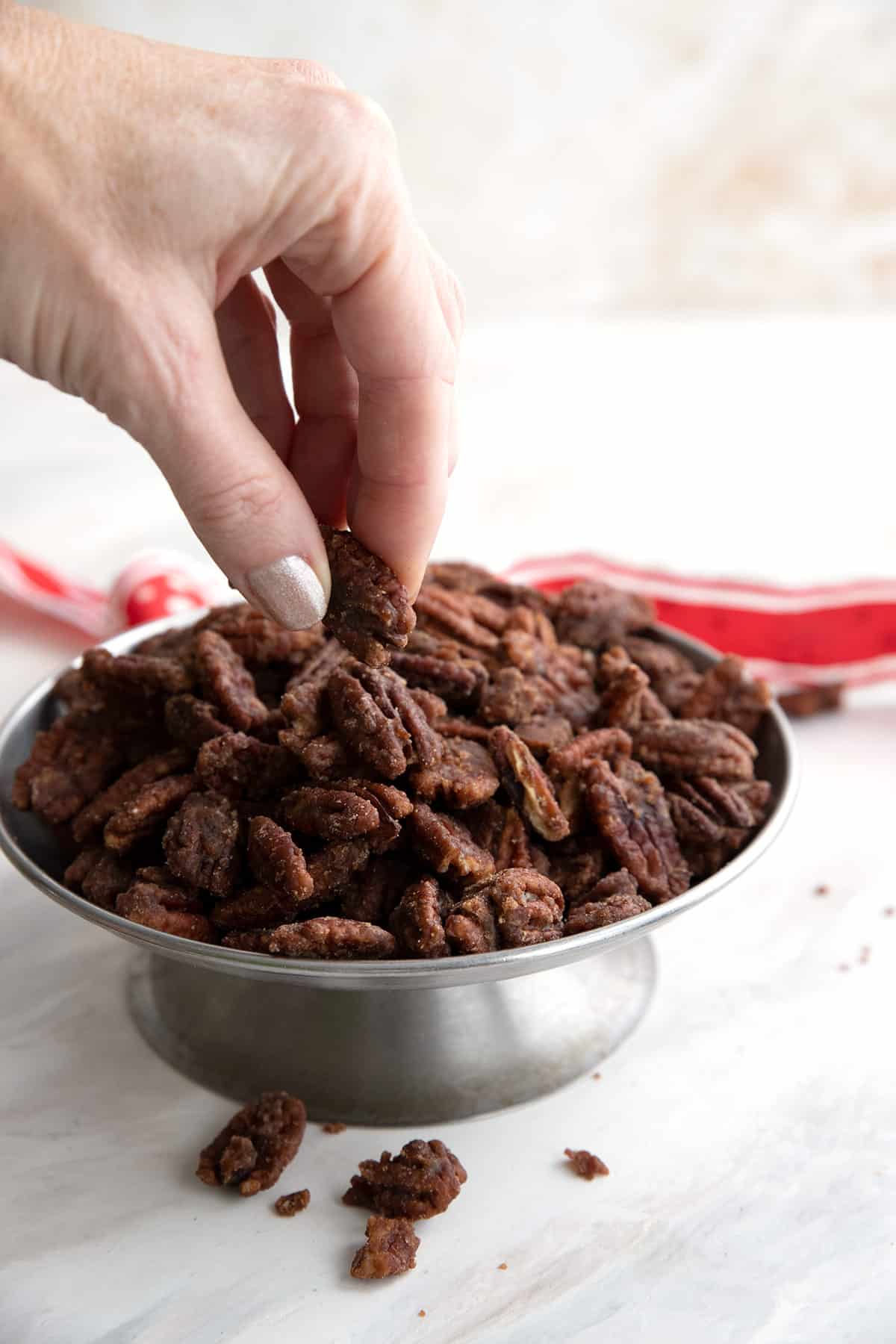 A hand reaching in to take keto candied pecans off a serving plate.