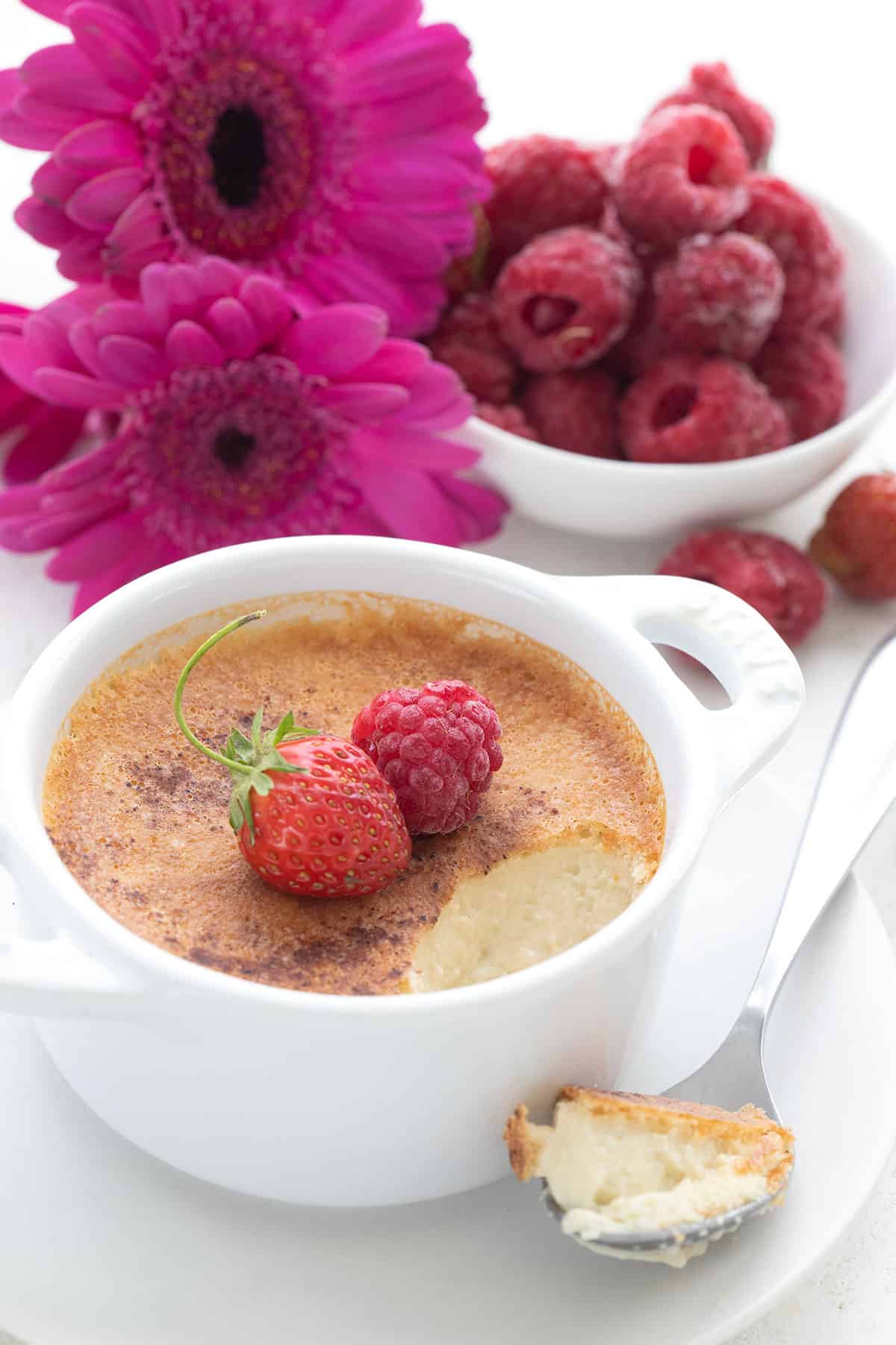 Baked keto custard in a white ramekin with pink flowers in the background.