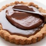 Titled image of a knife spreading chocolate over a Keto Caramel Cookie Tart.