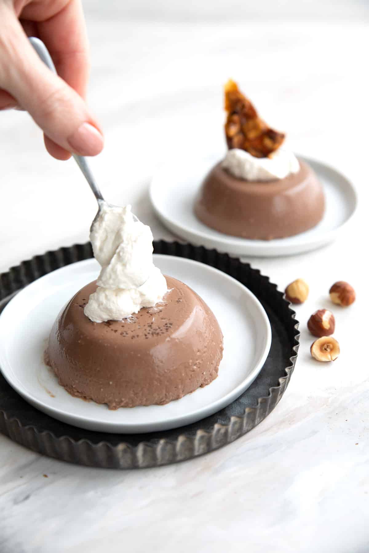 A hand dolloping whipped cream onto chocolate panna cotta.