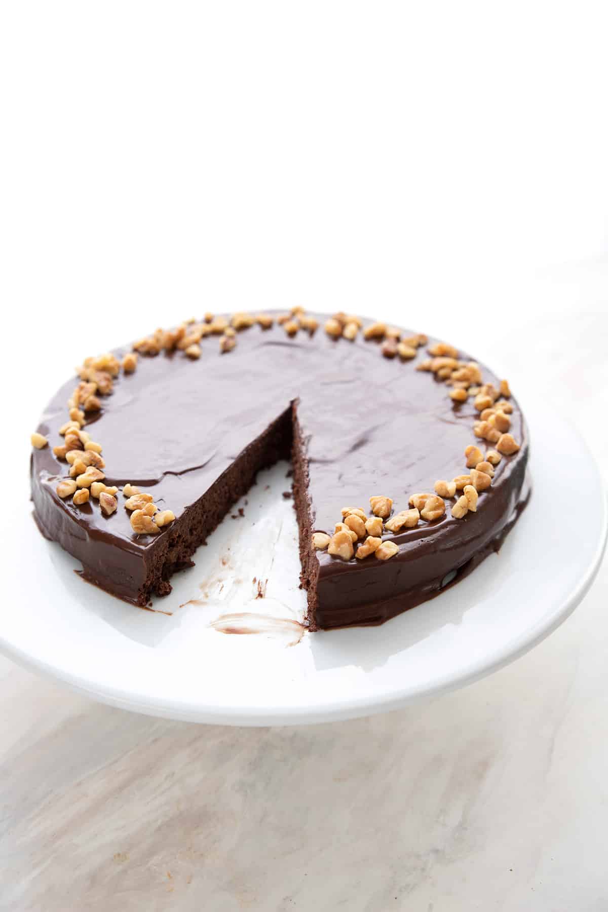 Chocolate walnut torte on a white cake plate with a slice taken out of it.