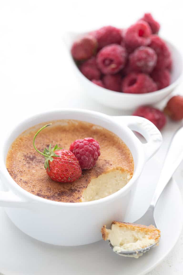 Keto Custard in a white ramekin with a spoonful taken out of it. A bowl of raspberries in the background.