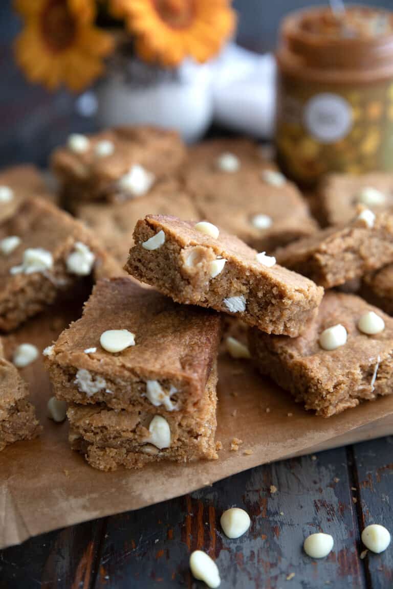 Keto Cookie Butter Bars piled on a wooden cutting board on a weathered wooden table.