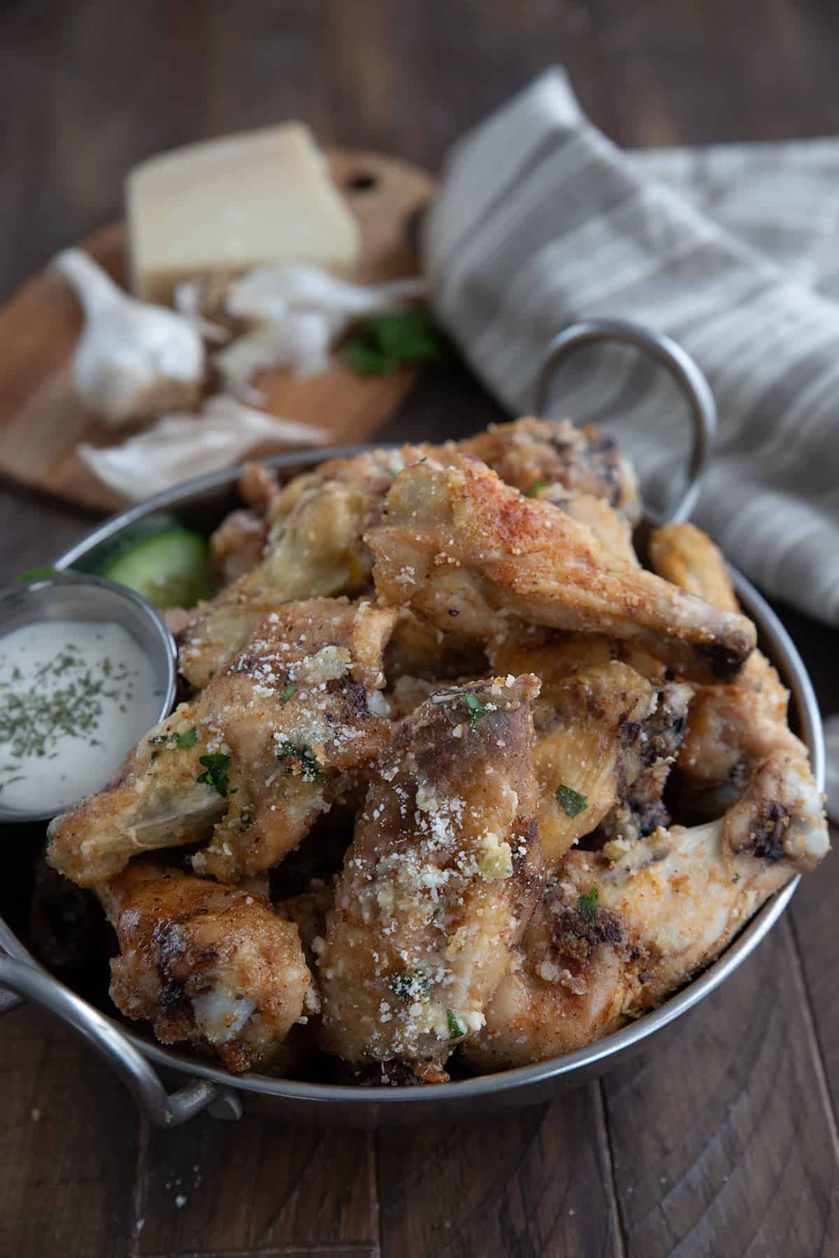 Keto Garlic Parmesan Wings in a metal bowl with garlic and parmesan in the background.