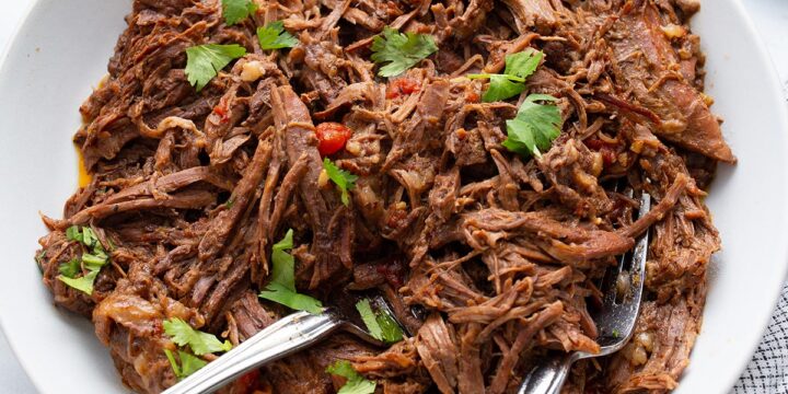 Mexican shredded beef in a white bowl on a marble table top.