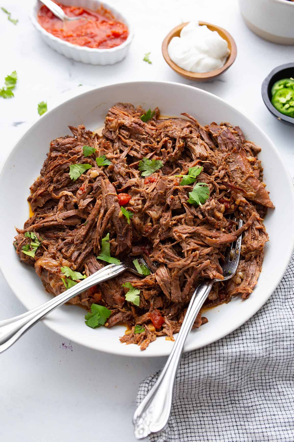 Mexican shredded beef in a white bowl on a marble table top.