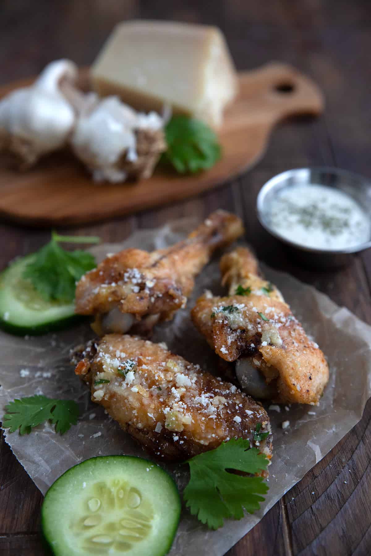 Three keto chicken wings on a piece of waxed paper with cucumbers and parsley.
