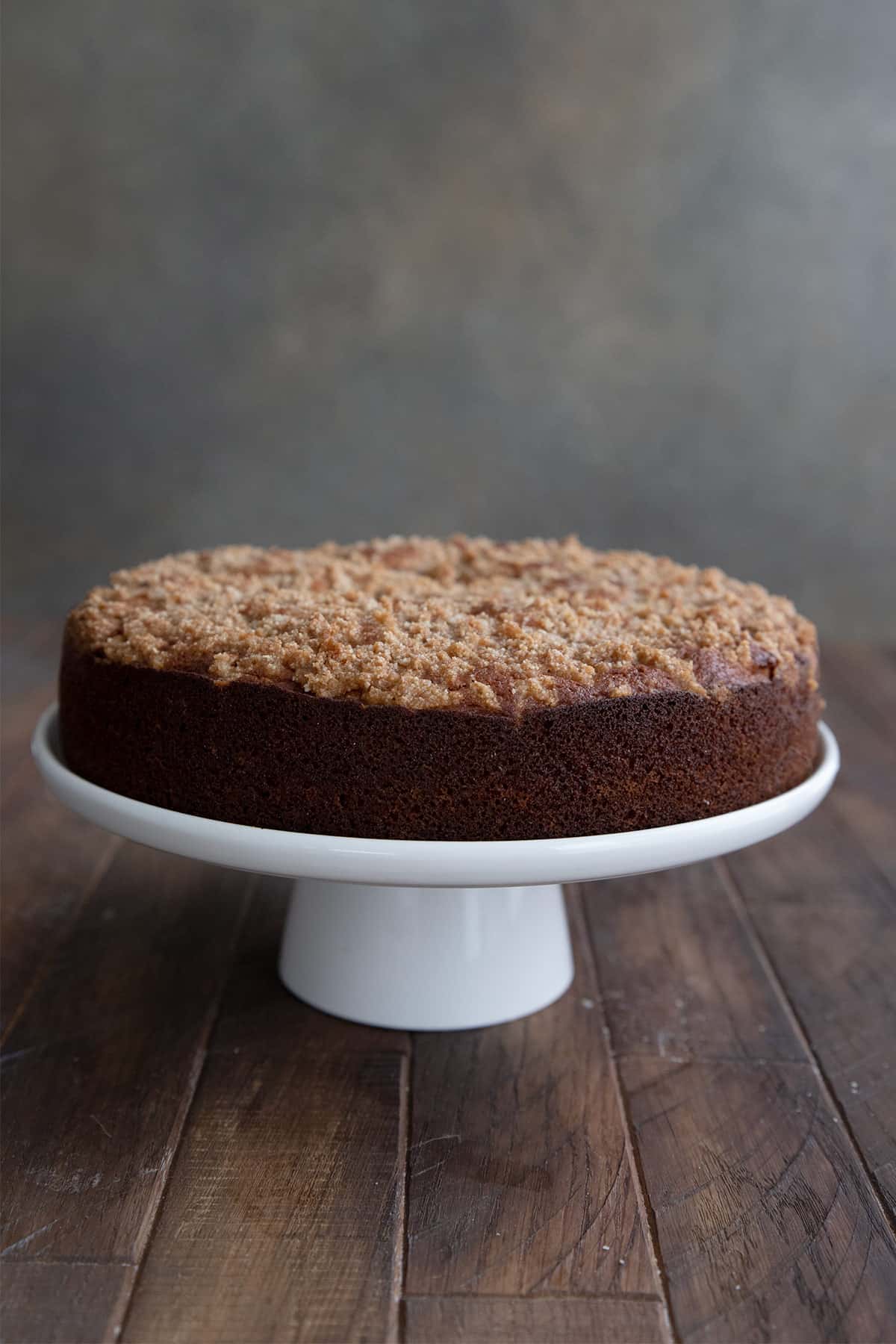 Keto sour cream coffee cake on a white cake plate on a wooden table.