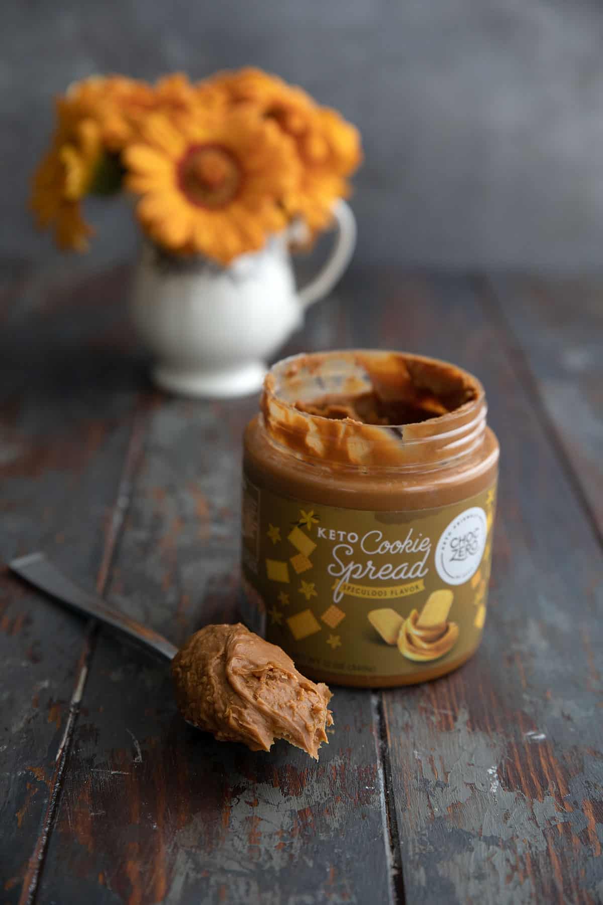 Keto cookie butter spread on a weathered wooden table with a vase of flowers in the background.