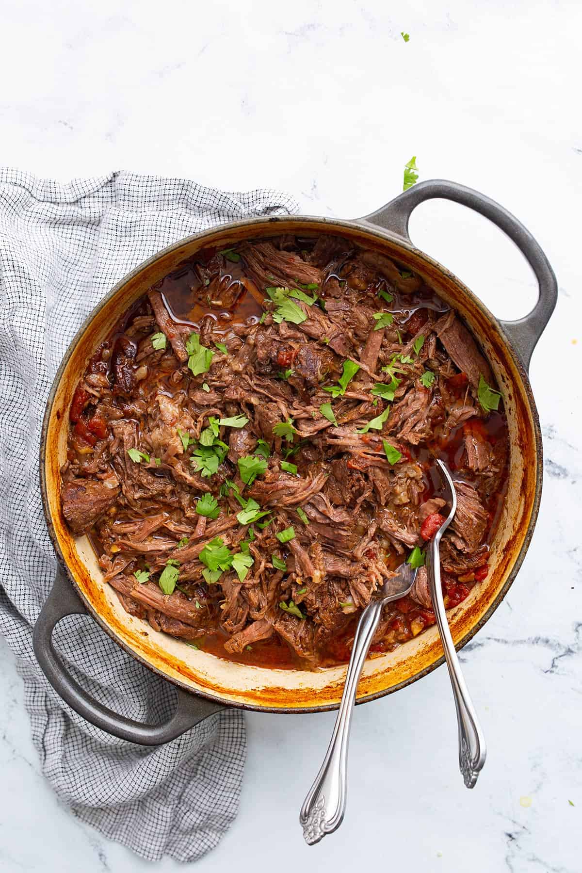 Top down image of Mexican Shredded Beef in a dutch oven with two forks in it.