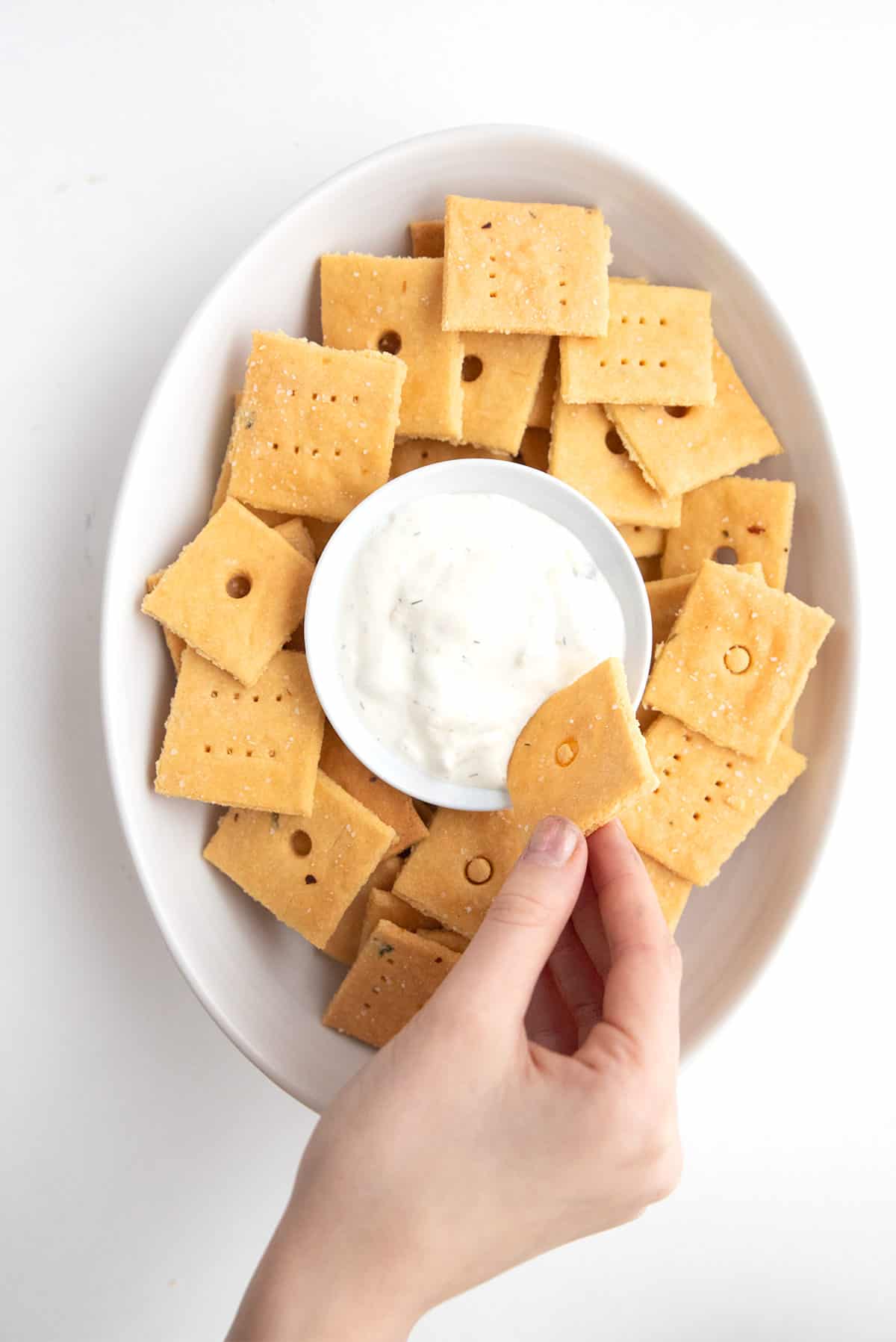 A hand dipping easy keto cheese crackers into a bowl of ranch dressing.