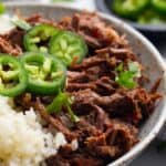 Titled Pinterest image of Mexican shredded beef in a bowl with cauliflower rice and jalapeño slices.