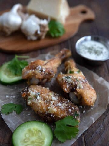 Three keto chicken wings on a piece of waxed paper with cucumbers and parsley.