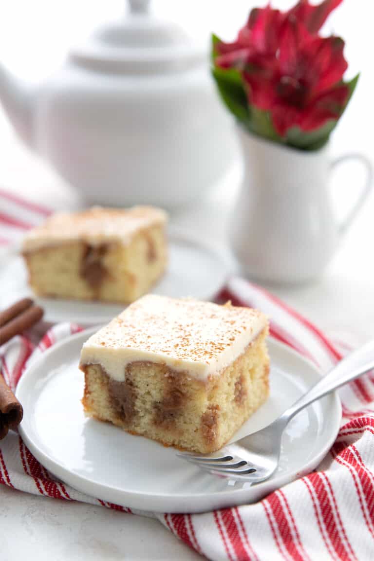 A slice of keto cinnamon roll cake sits on a white plate over a red striped napkin.