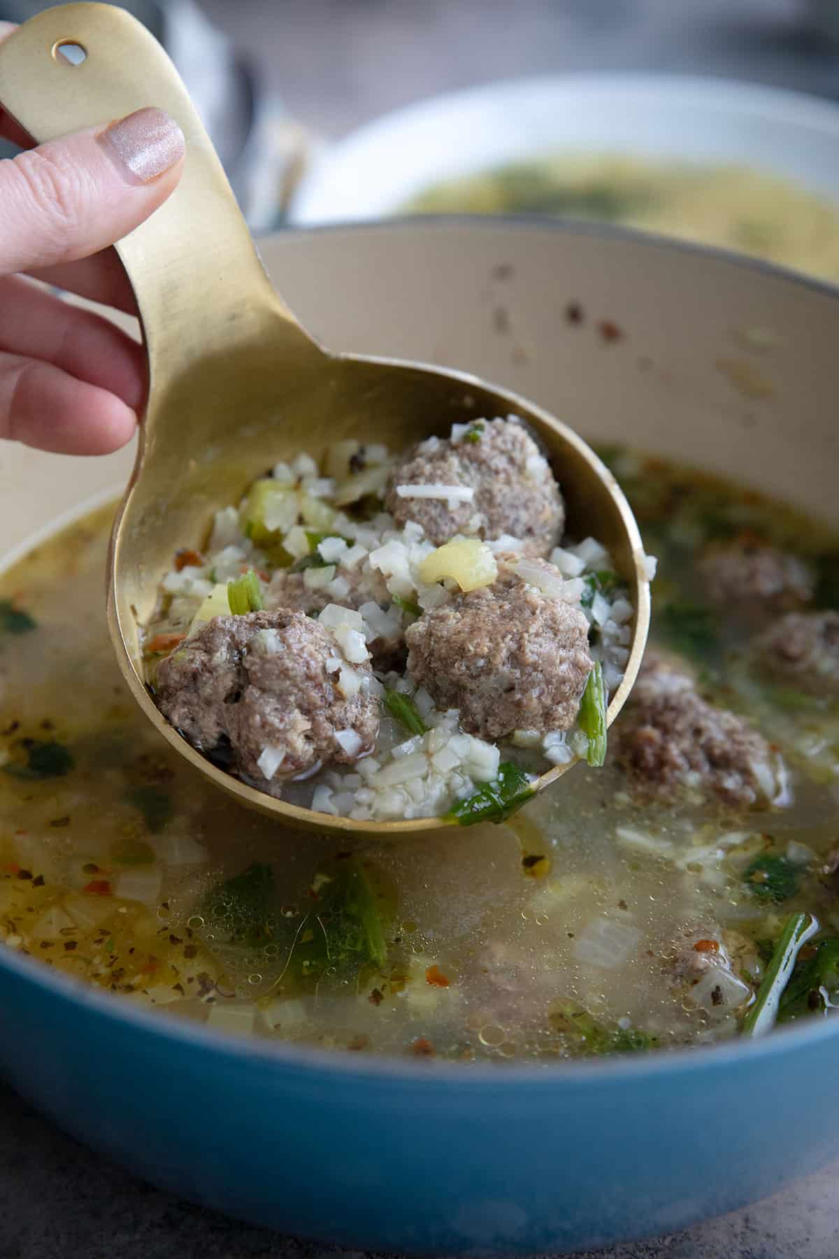 A ladle filled with Italian wedding soup over the pot of soup.