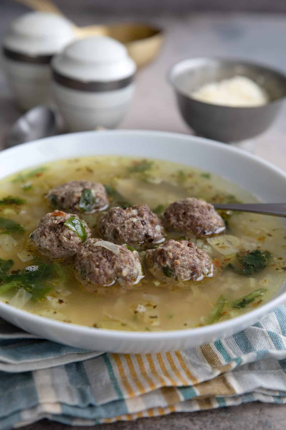 A white bowl filled with Italian Wedding Soup over a striped napkin.