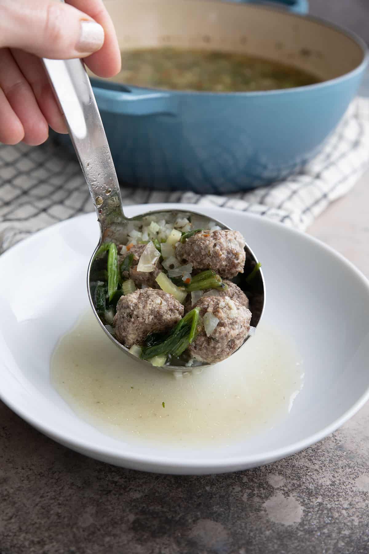 A ladle filling a white bowl with Keto Italian Wedding Soup with cauliflower rice.