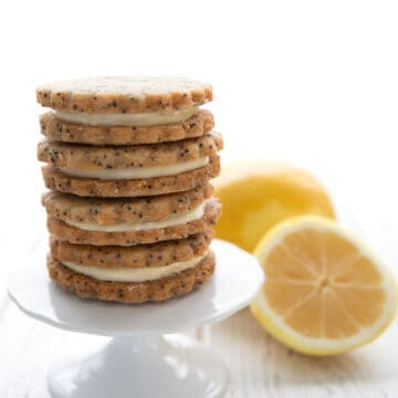 A stack of keto lemon sandwich cookies on a white cupcake stand with lemons in the background.