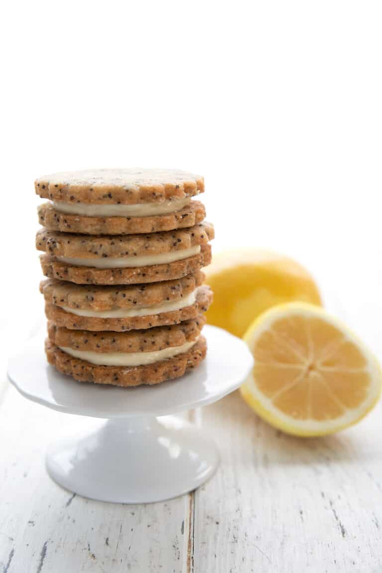 A stack of keto lemon sandwich cookies on a white cupcake stand with lemons in the background.