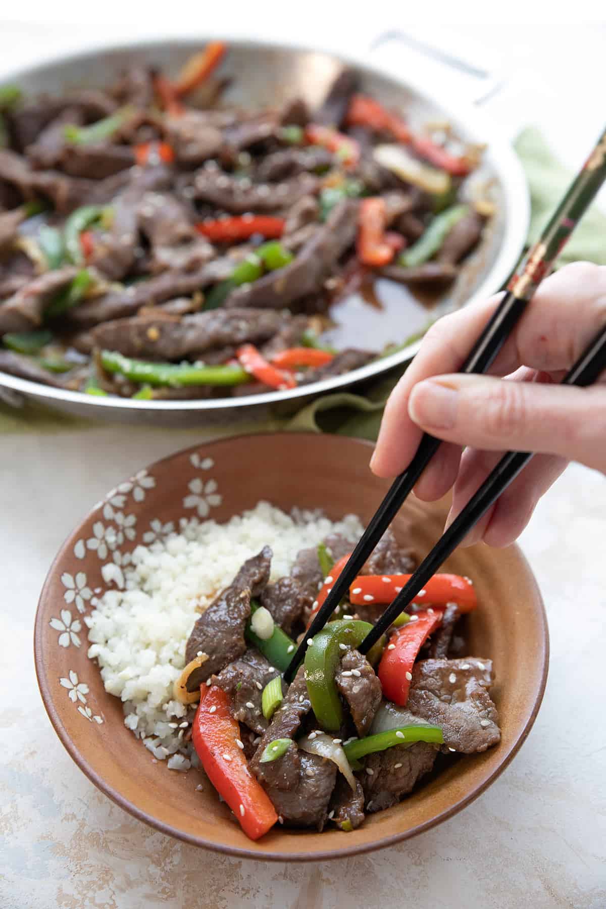 A hand reaching in with chopsticks to take a bite of Pepper Steak Stir Fry.