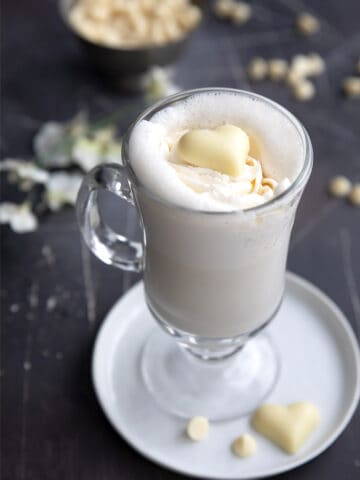 A tall glass mug filled with Keto White Hot Chocolate with a white chocolate heart on top.