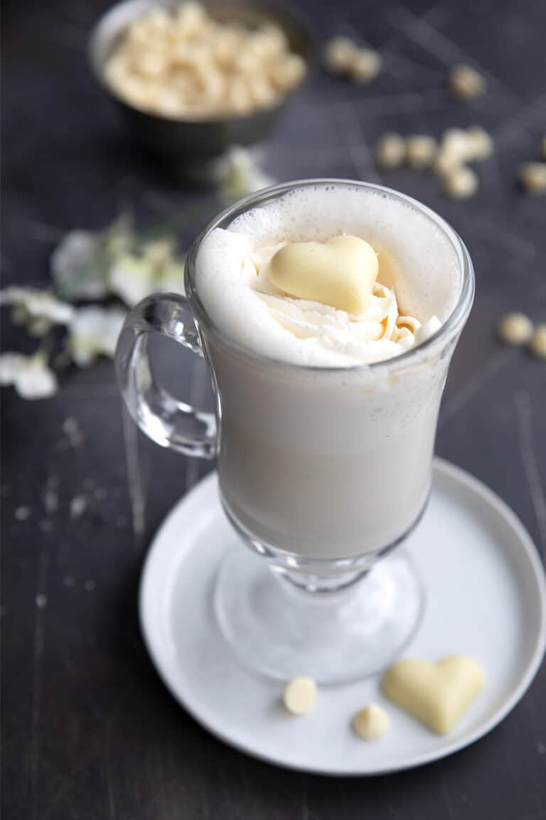 A tall glass mug filled with Keto White Hot Chocolate with a white chocolate heart on top.