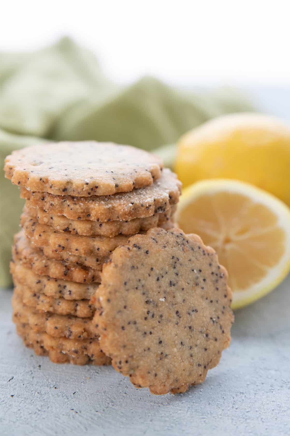A stack of keto lemon poppy seed cookies with some lemon in the background.
