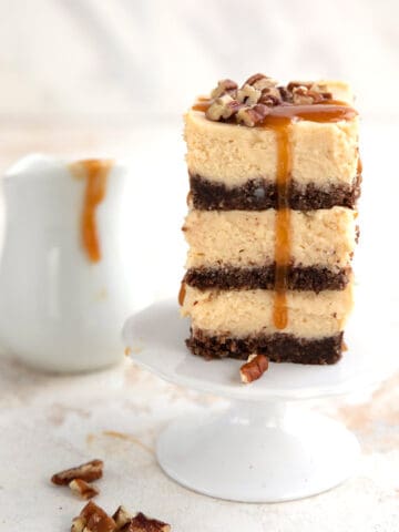 A stack of keto caramel cheesecake bars with a small pitcher of caramel sauce in the background.