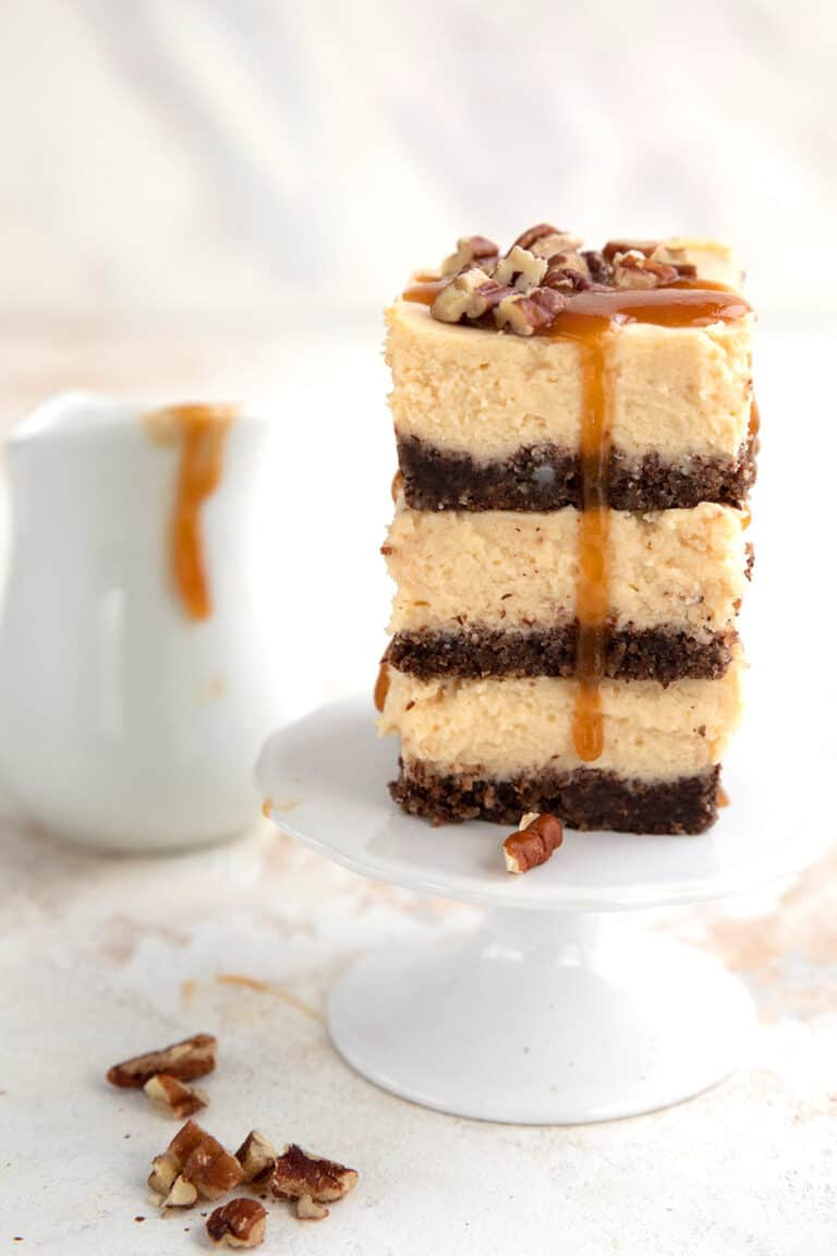 A stack of keto caramel cheesecake bars with a small pitcher of caramel sauce in the background.