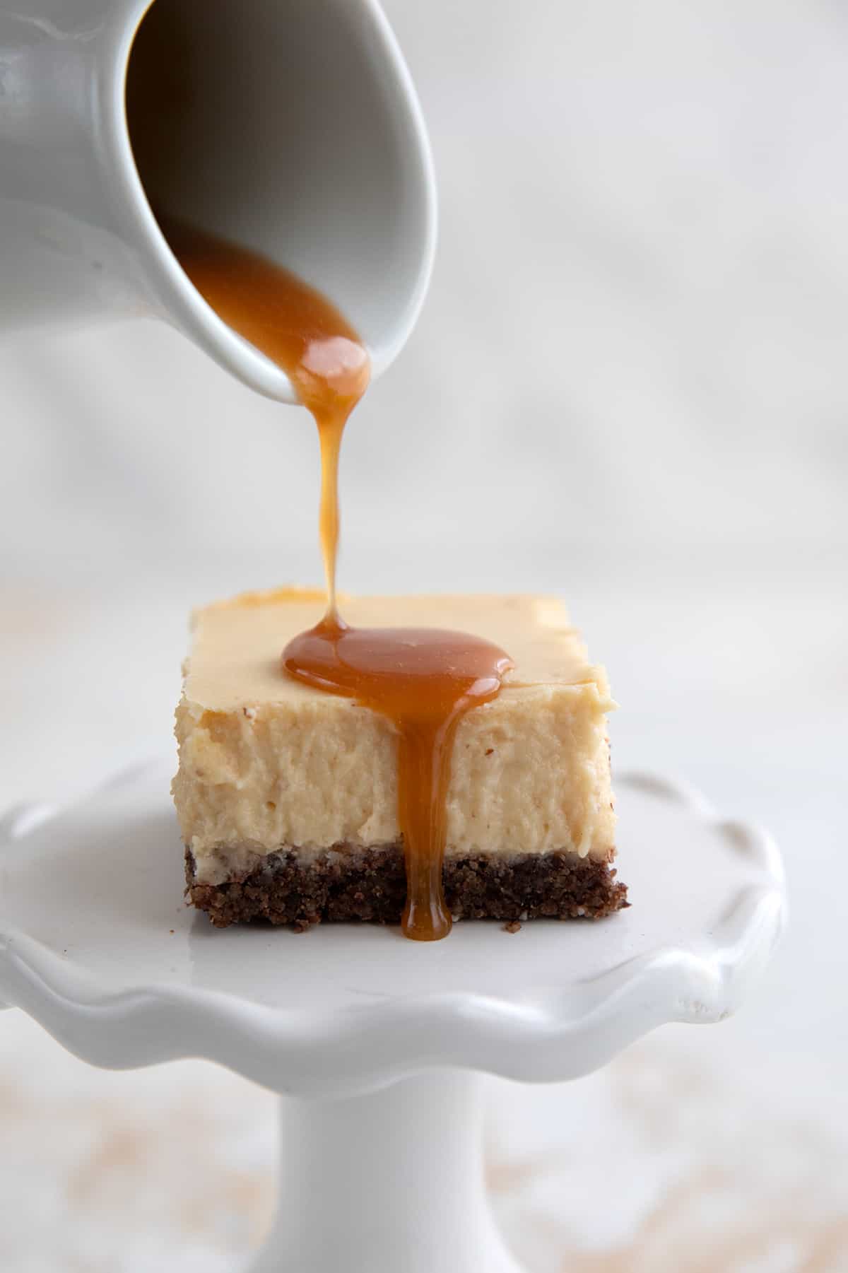 Keto caramel sauce being poured over a cheesecake bar.