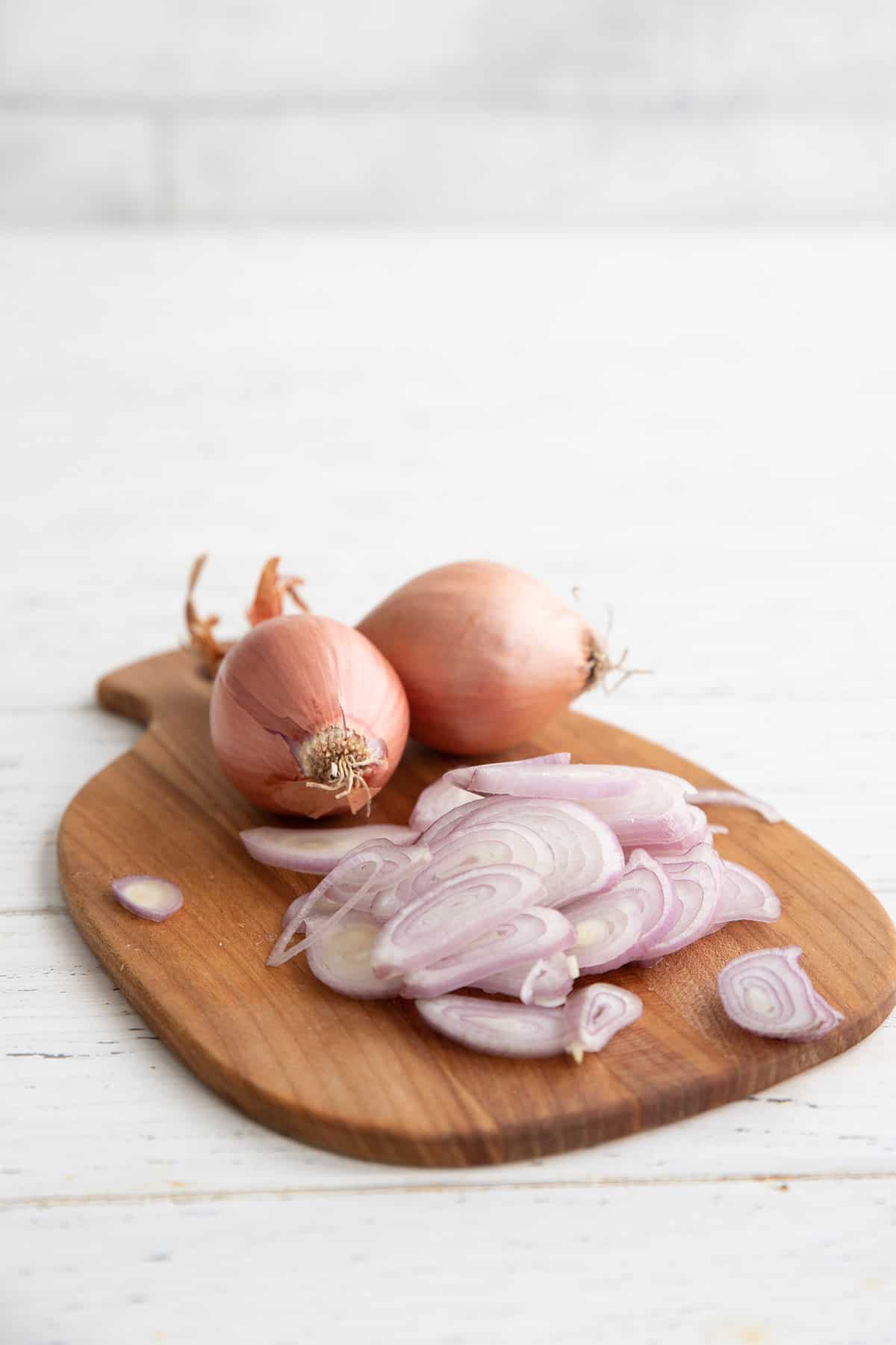 Two whole shallots with a sliced shallot sitting on a small cutting board.