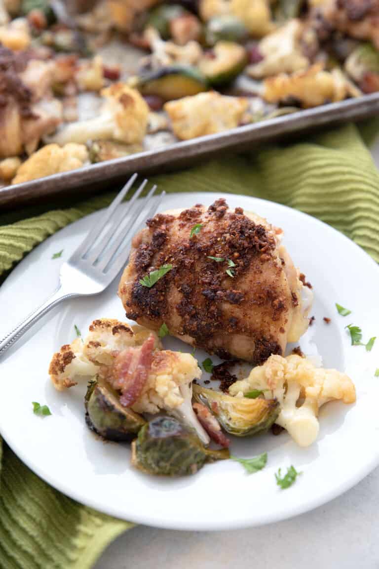 A white plate full of sheet pan chicken and veggies in front of the pan.