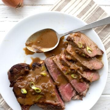 Top down image of sliced steak Diane on a white plate with a spoonful of sauce on the side.