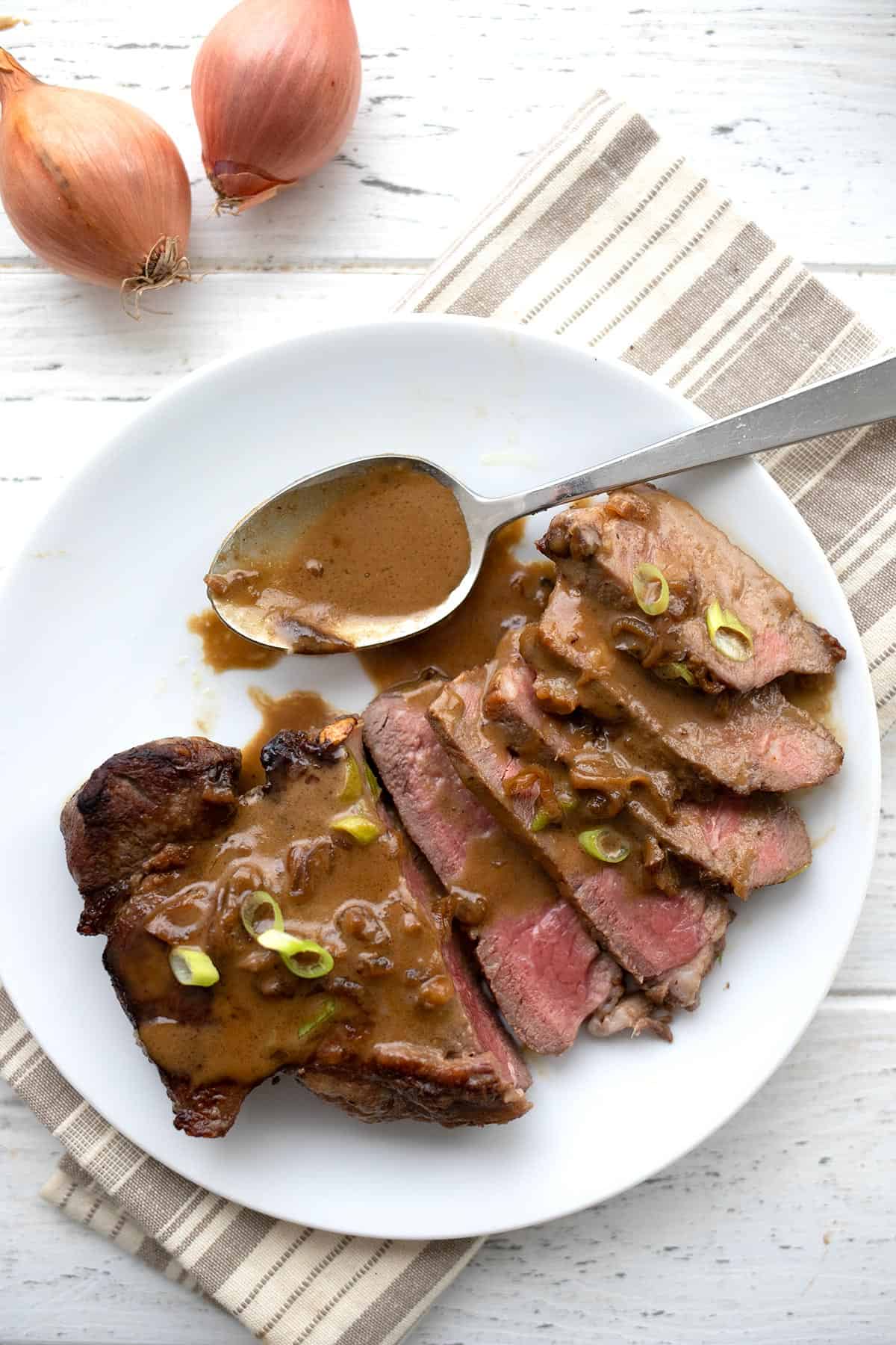 Top down image of sliced steak Diane on a white plate with a spoonful of sauce on the side.
