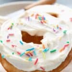 Titled image of Keto Vanilla Protein Donuts on a white plate over a teal patterned napkin.