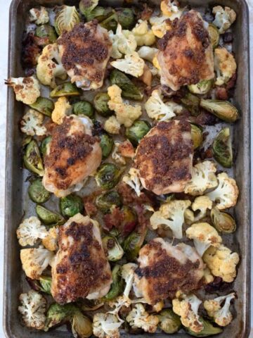 Top down image of sheet pan chicken thighs with cauliflower and Brussels sprouts.