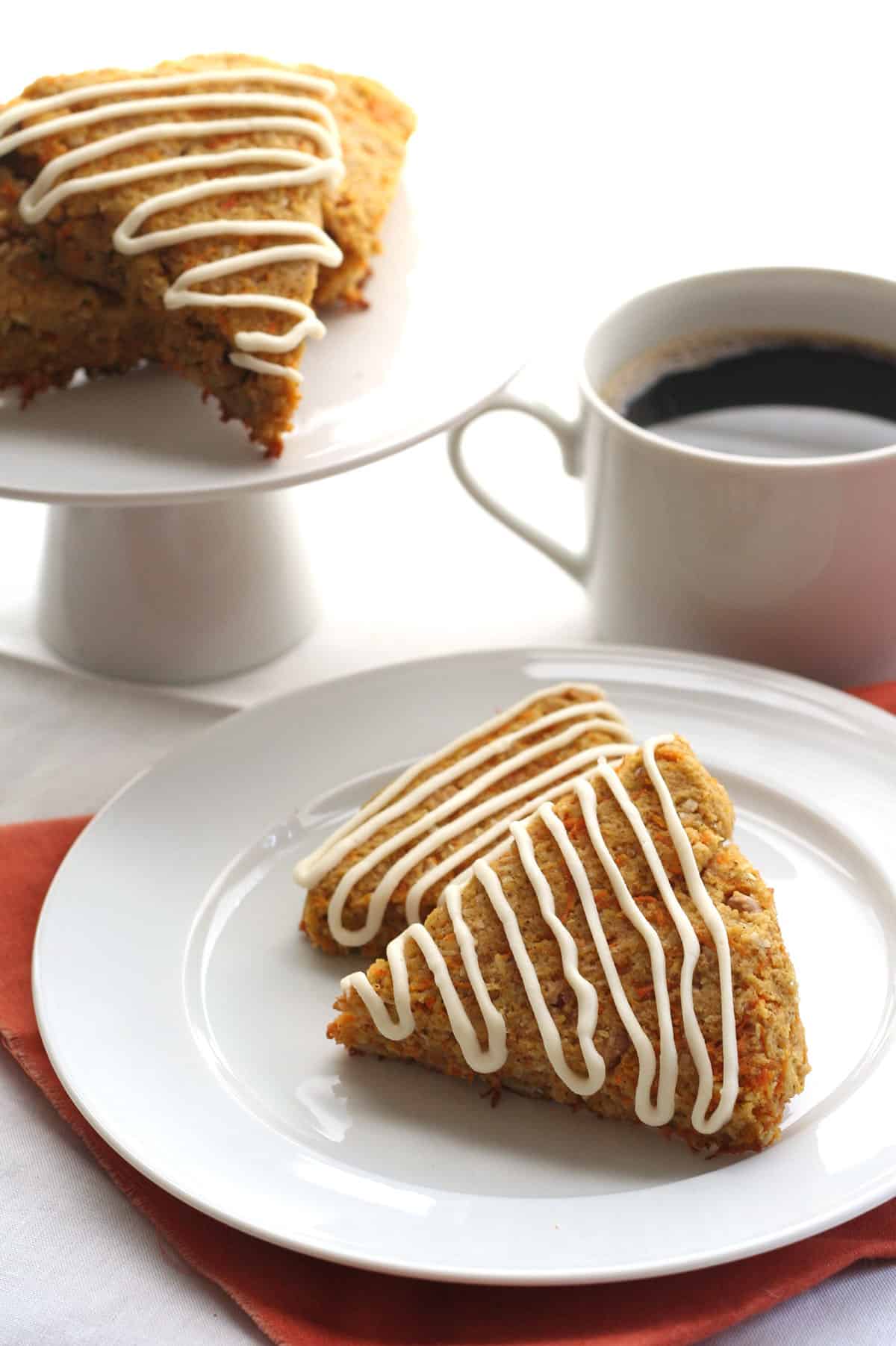 Two keto carrot cake scones on a white plate in front of a cup of coffee.
