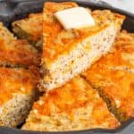 Titled image of a slice of cheesy keto skillet bread with butter on top, resting on the rest of the bread in the pan.