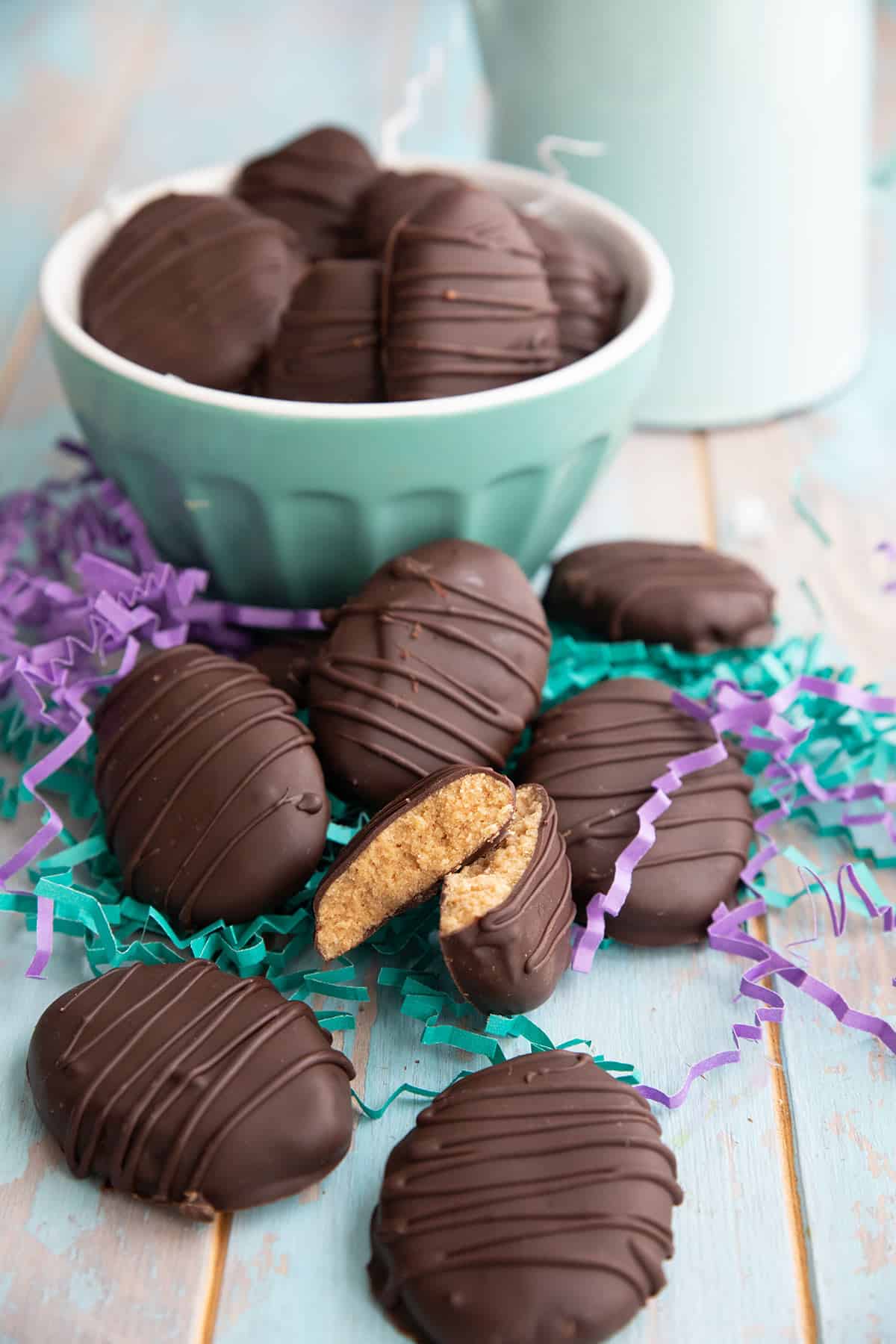 Keto Peanut Butter Eggs in a pile on a wooden table with one broken open to show the inside.