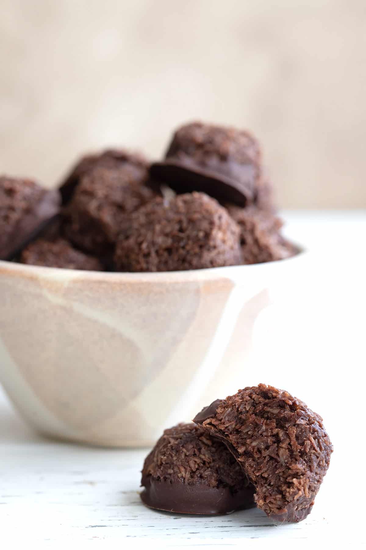 Two keto chocolate macaroons sitting in front of a bowl of more macaroons.