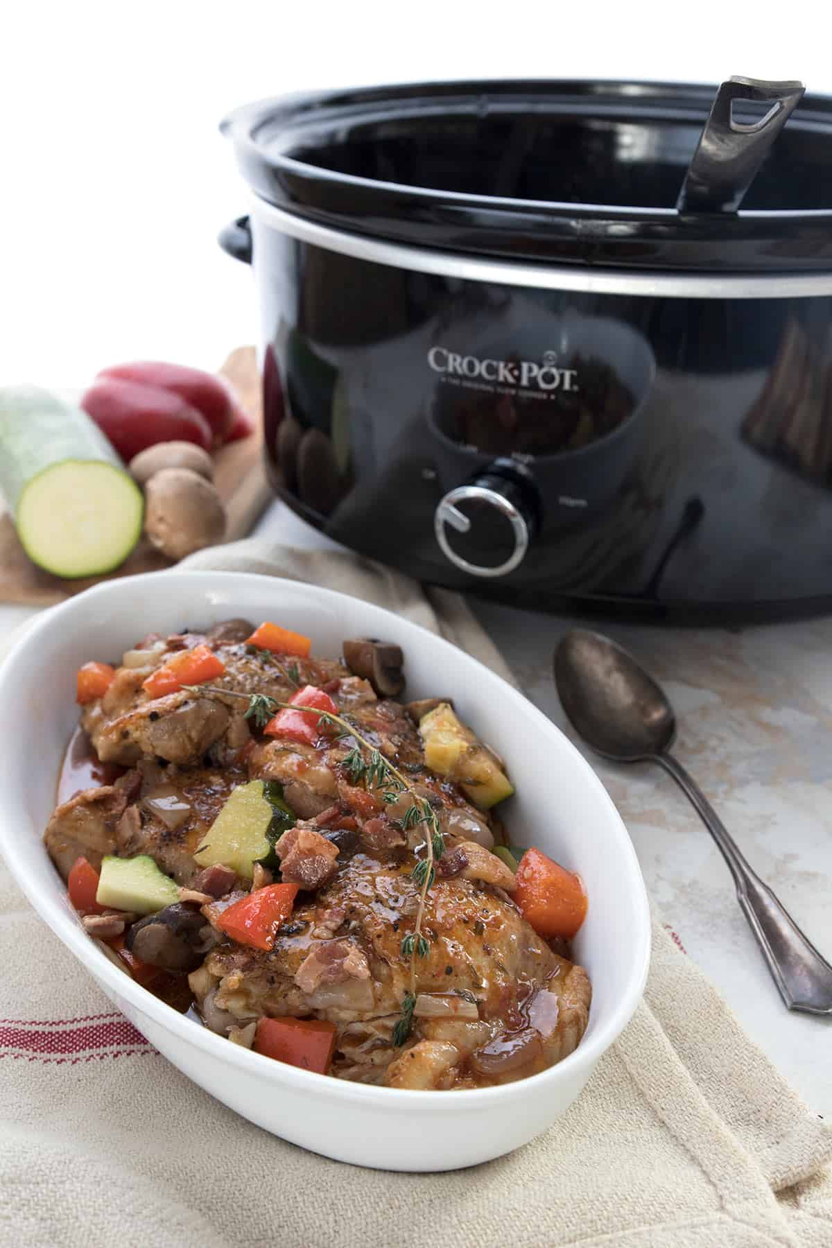 Coq au Vin in a white oval dish in front of a slow cooker.