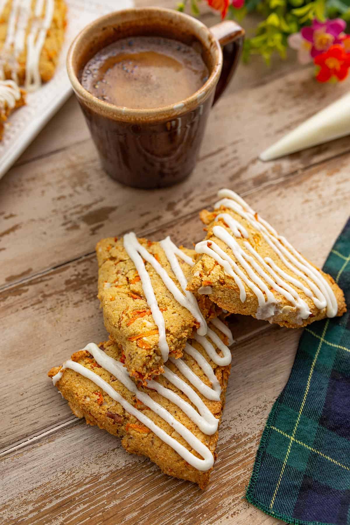 A pile of keto carrot cake scones on a wooden table with a cup of coffee.