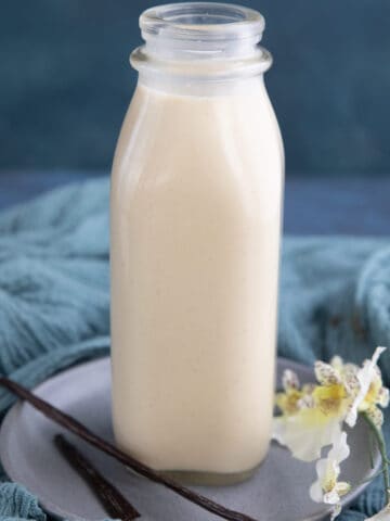 Keto low carb coffee creamer in a glass bottle with vanilla beans in front.