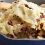 Titled image of Keto Reuben Casserole in a blue skillet, with some being lifted up on a wooden spoon.