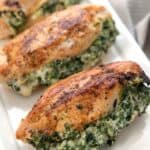 Four spinach stuffed chicken breasts on a rectangular white platter.