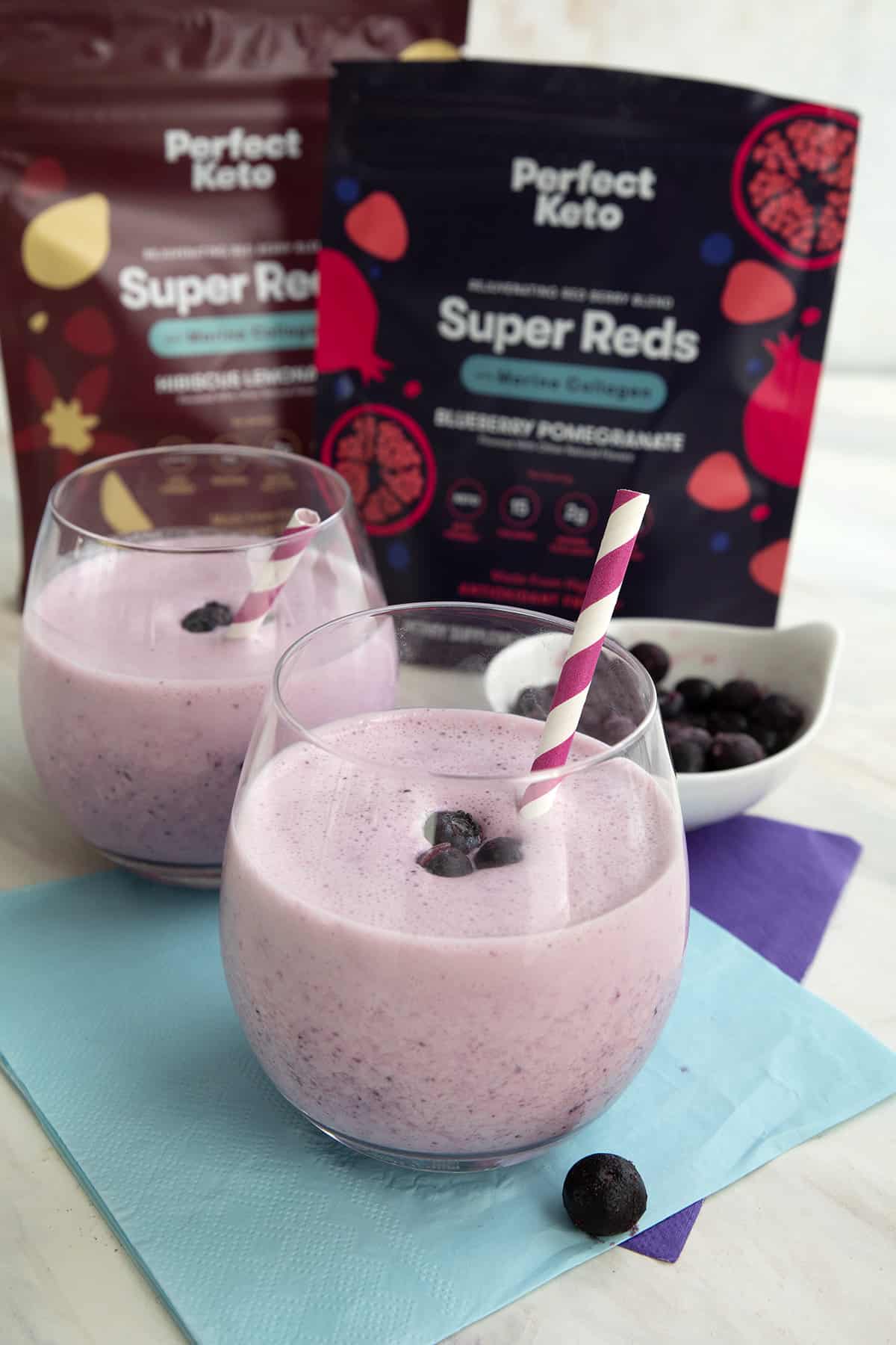 Keto blueberry smoothies with packages of Super Reds antioxidant blend in the background.